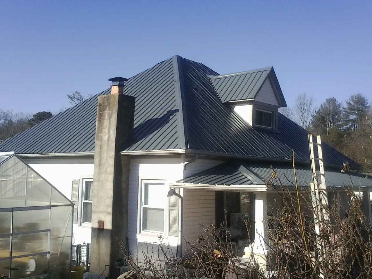 Dark blue standing seam metal roof on a white farmhouse with dormer — Slate & Tile Roof Repair by Roofing Brothers in New Knoxville