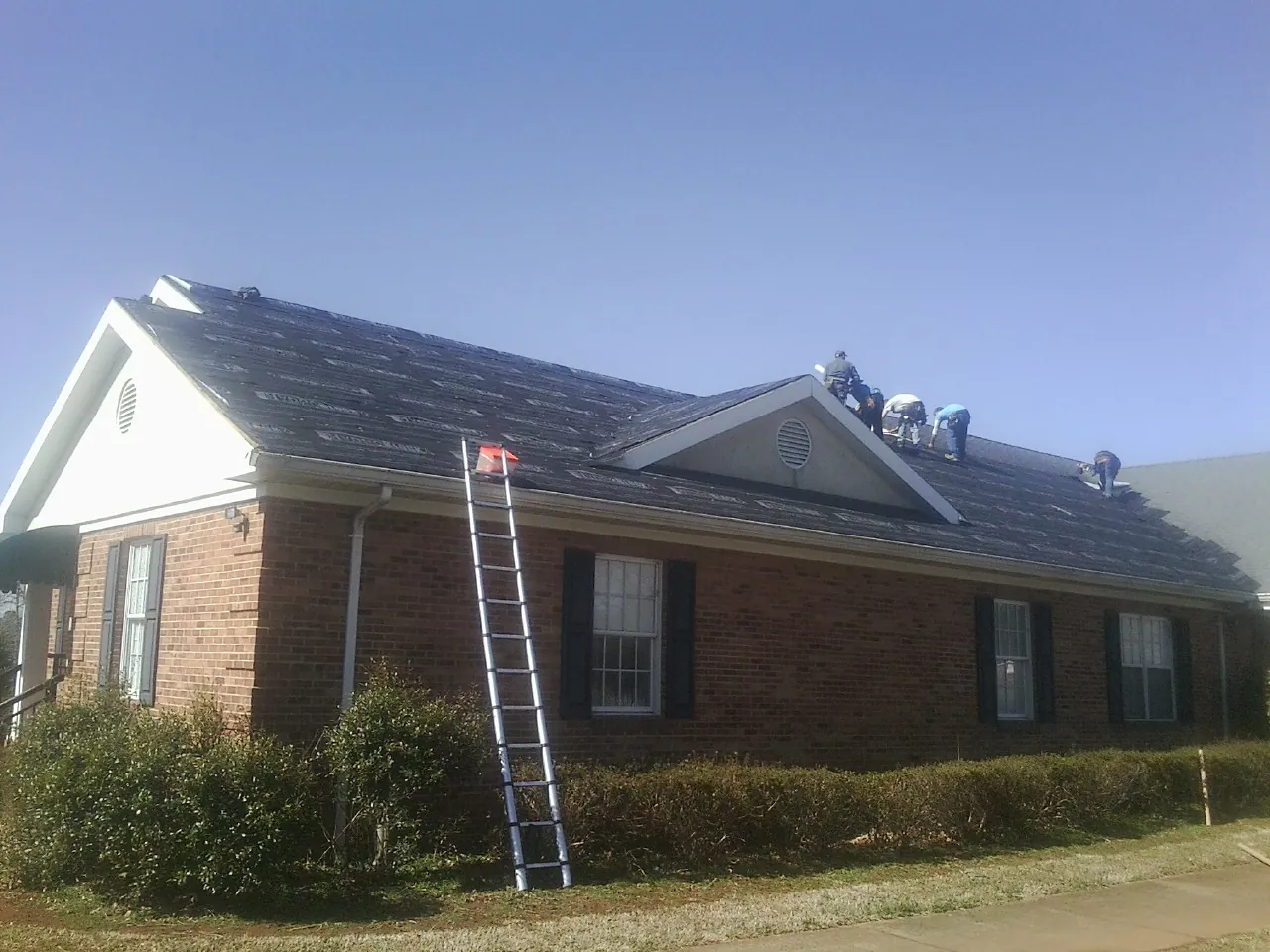 Crew tearing shingles off a brick ranch roof with a ladder set — Emergency Roof Repair work by our crew in New Knoxville