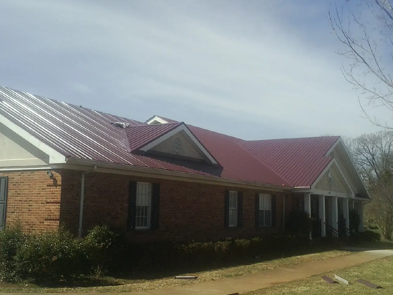 Red metal roof with gabled entries on a long brick building, from a Hail Damage Roof Repair job in New Knoxville