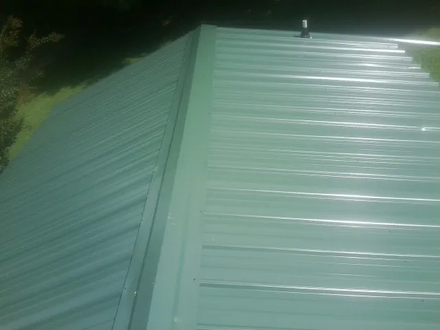 New green metal panels meeting at the ridge of a roof — Flat Roof Repair work by our crew in New Knoxville