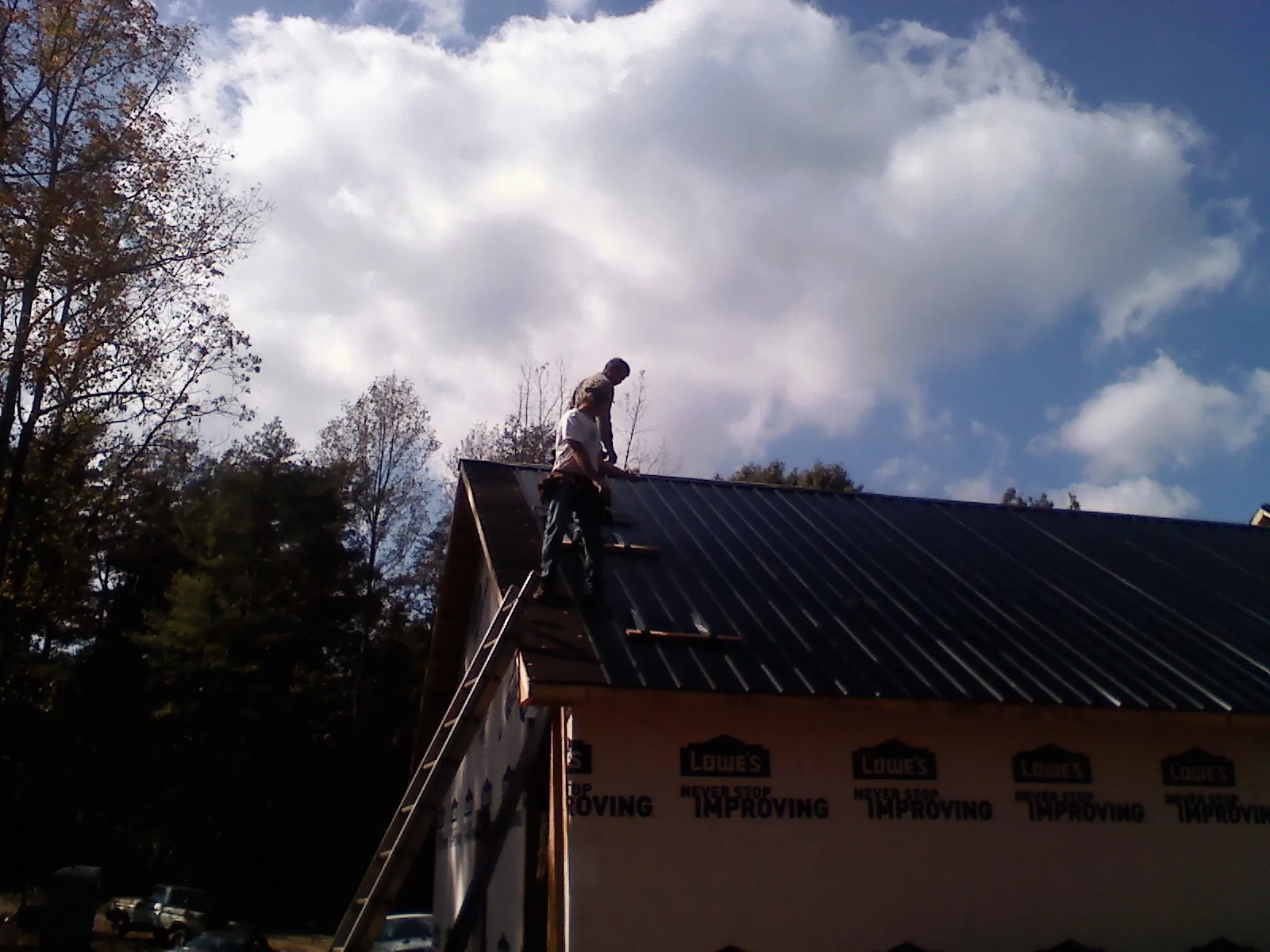 Roofer fastening dark metal panels high against a cloudy sky, from a Roof Inspection job in New Knoxville