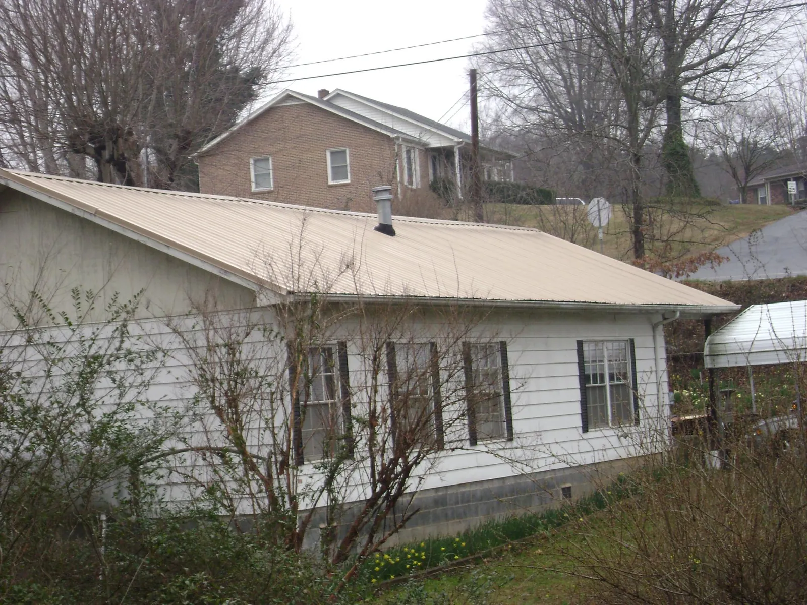 Tan metal roof on a white sided house set into a hillside — Commercial Roofing by Roofing Brothers in New Knoxville